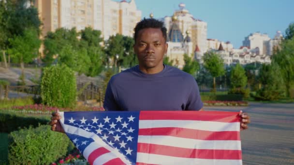 Portret van een Afro-Amerikaanse man met een Amerikaanse vlag en kijkt camera in de zomer — Stockvideo