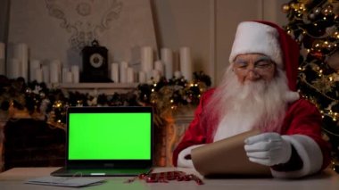 Gülümseyen Noel Baba hediye listesi ve dizüstü bilgisayarlı yeşil ekranlı mektubu okuyor.