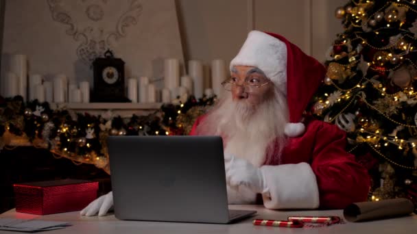 Przemyślany współczesny Mikołaj używa laptopa kupuje prezenty świąteczne w Internecie — Wideo stockowe