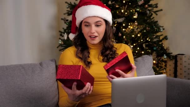 Kobieta w kapeluszu Santa Claus otwiera pudełko prezentów i zaskoczony, online wideo rozmowy laptop — Wideo stockowe