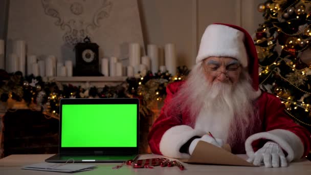 Święty Mikołaj pisze gratulacje dla dzieci na Nowy Rok, laptop zielony ekran — Wideo stockowe