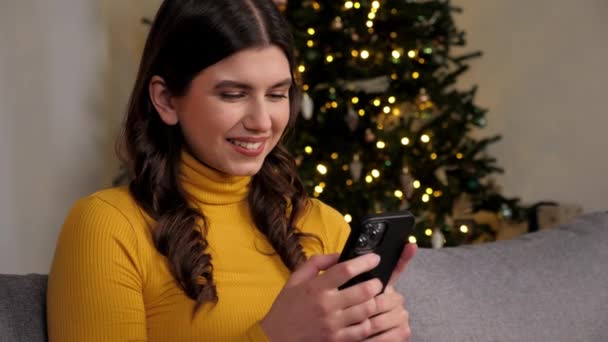 Usmívající se žena kupuje novoroční dárky na internetu pomocí smartphone, vánoční stromeček — Stock video