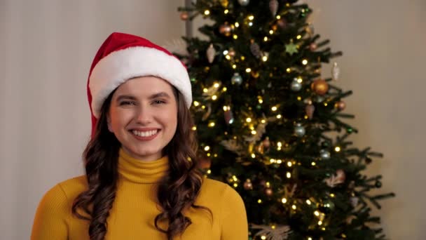 Portrét usmívající se žena v klobouku Santa Claus vypadá fotoaparát doma, vánoční strom — Stock video
