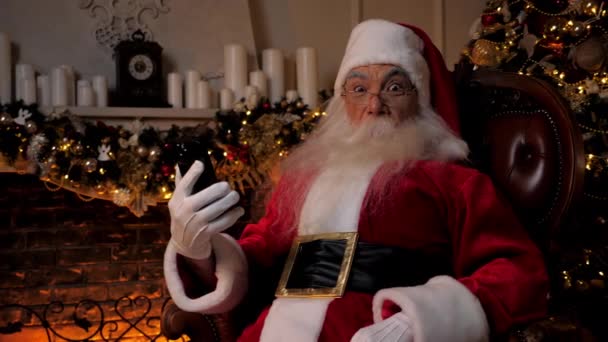 Shocked Santa Claus mira el teléfono inteligente, gira la cabeza en la cámara de miradas sorpresa — Vídeos de Stock