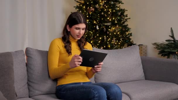 Hermosa mujer gamer jugando juego en la tableta en el árbol de Navidad de fondo — Vídeo de stock