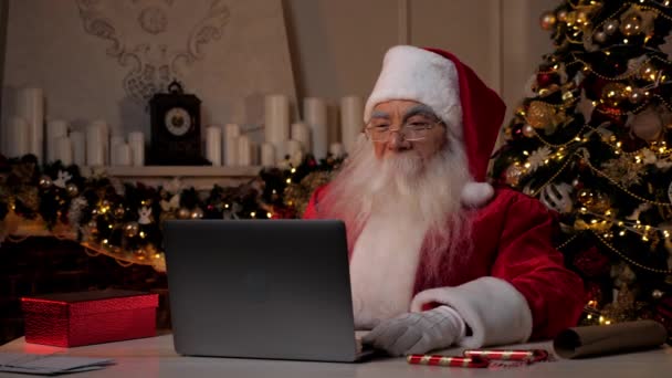 Усмішка Санта Клауса використовує ноутбук, читаючи лист з переліком подарунків від дітей. — стокове відео