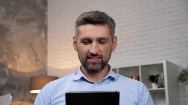 Крупным планом улыбающийся бизнесмен пользуется планшетом в домашнем офисе — стоковое видео