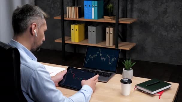 Человек брокер прокрутки планшет с биржевой графикой, ноутбук с фондовым рынком — стоковое видео