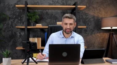 Gülümseyen adam hisse senedi tüccarı yatırımcıyı internetten dinler, not defterine notlar alır.