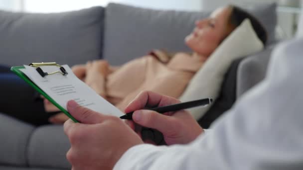 Close up man psychotherapist taking notes on clipboard and listen woman patient — Stock Video