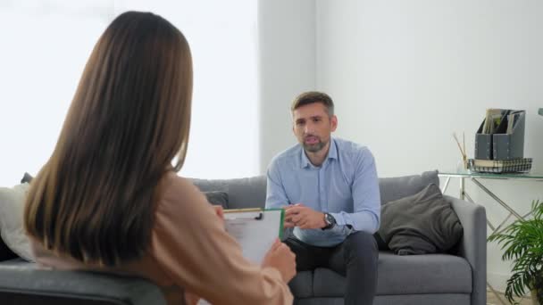 Homem paciente com problemas de saúde mental sentado no sofá conversando com o terapeuta — Vídeo de Stock