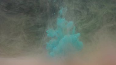 Slow motion turquoise blue ink mixing in water with colored acrylic paint