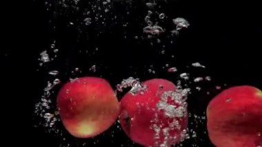 Slow motion three red apple falling into transparent water on black background