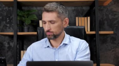 Businessman inserts wireless earphones into ears, works for laptop in office