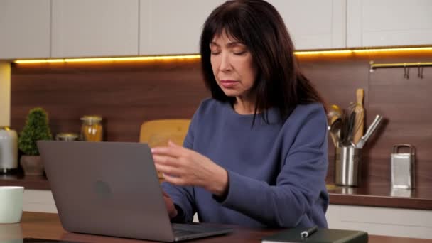 Tired aged woman works for laptop rubs eyes after long hard work at computer — Wideo stockowe