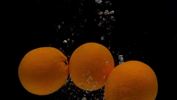 Yavaş çekim üç portakal siyah zemin üzerinde şeffaf suya düşüyor — Stok video