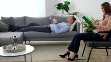 Ruhsal sorunları olan üzgün yetişkin bir adam kanepede uzanıp terapistle konuşuyor.