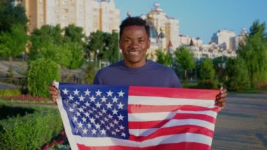 Portre mutlu Afrikalı yetişkin erkek etnik zenci Amerikan bayrağıyla park yerinde duruyor