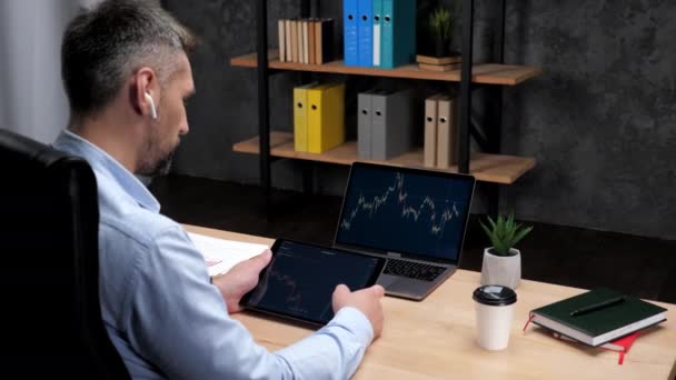 Man broker scrollen tablet met aandelenbeurs grafiek, laptop met aandelenmarkt — Stockvideo