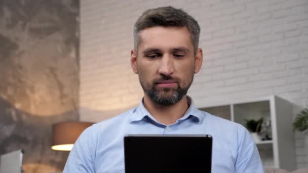 Крупным планом улыбающийся бизнесмен пользуется планшетом в домашнем офисе — стоковое видео