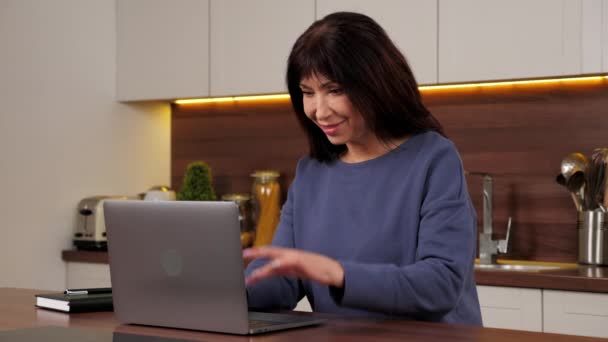Gülümseyen iş kadını, ev mutfağında yoğun bir günün ardından dizüstü bilgisayarı kullanmayı bırakıyor. — Stok video