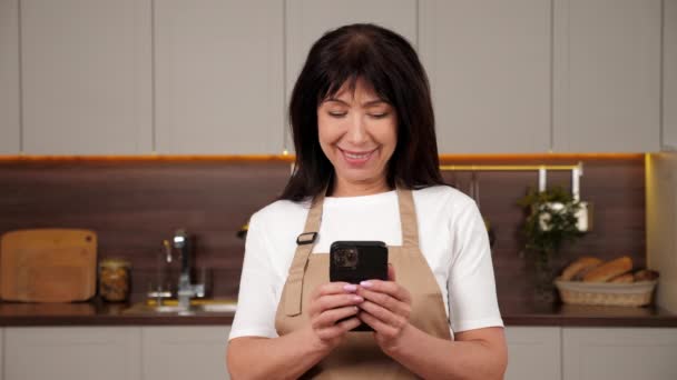 Sorridente donna anziana chef utilizza smartphone in casa cucina moderna — Video Stock