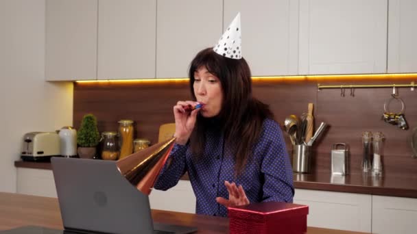 Starší žena ve stranickém klobouku otevře červenou dárkovou krabici a je překvapen v domácí kuchyni — Stock video