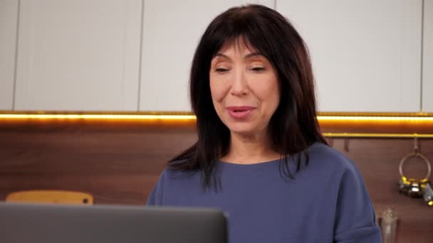 Leende kvinna hälsar talar online videosamtal webbkamera laptop i köket — Stockvideo