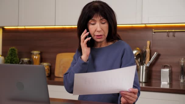 Bizneswoman rozmawiając przez telefon komórkowy posiada roczny raport sprzedaży w kuchni domowej — Wideo stockowe