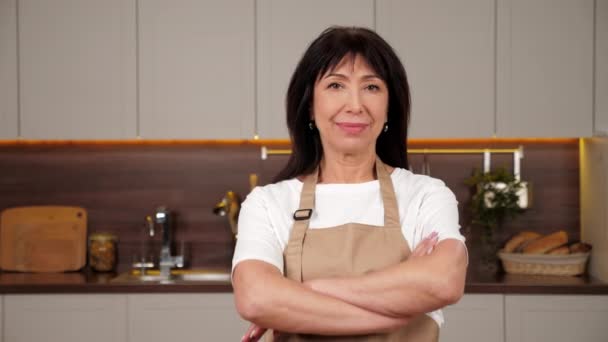 Portrait femme âgée souriante chef croise les mains et regarde caméra dans la cuisine de la maison — Video