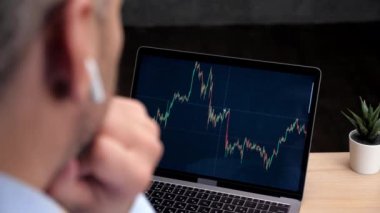 Düşünceli borsa simsarı dizüstü bilgisayarını borsa ekran grafiği ile kullanıyor.