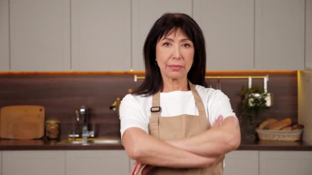 Portrét usmívající se stará žena kuchař kříží ruce a vypadá kamera v domácí kuchyni — Stock video
