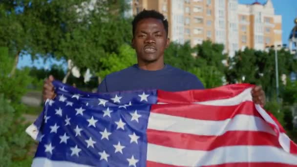 Portrait Afro-American man holding American flag looks camera says USA in summer — Stock videók