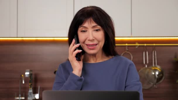 Närbild leende äldre kvinna talar på mobiltelefon med familj i hemmet kök — Stockvideo