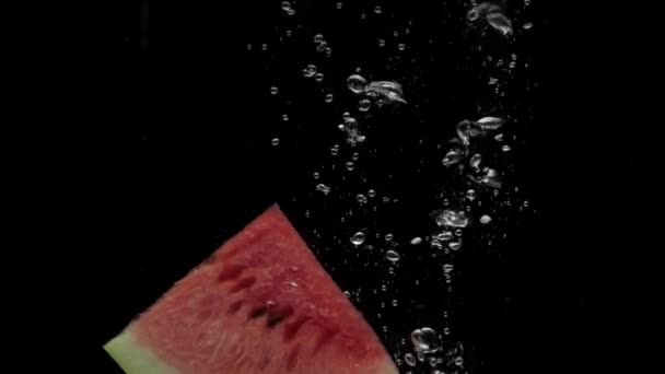 Slow motion skiva vattenmelon faller i transparent vatten på svart bakgrund — Stockvideo