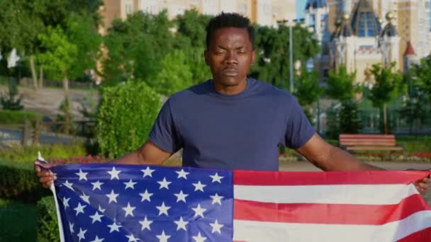 Camera zoom in patriot Afro-American man holding American flag and looks camera — Stock Video