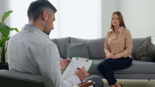 男性医師精神療法士リッスン患者取りノート上のクリップボードでクリニック — ストック動画