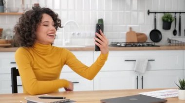 Gülümseyen kıvırcık kadın öğrenci selamlıyor. İnternetten video dinliyor. Akıllı telefon.