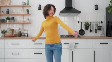 Mutfakta müzik dinleyip dans eden mutlu İspanyol kıvırcık kadın.