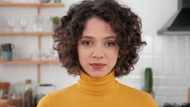 Gros plan visage hispanique bouclé femme regardant caméra debout à la maison cuisine — Video