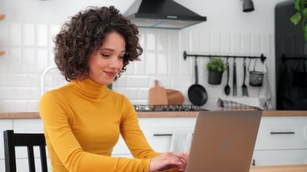 Çalışan gülümseyen öğrenci ev mutfağındaki klavyede dizüstü bilgisayar kullanıyor. — Stok video