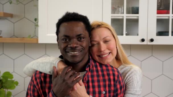 Portrait smiling multiethnic couple hugging looking camera at home kitchen — Vídeo de stock