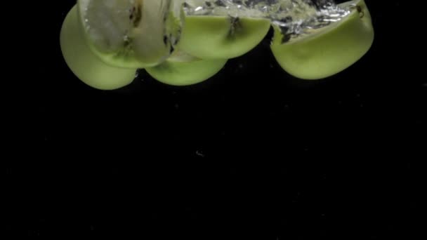 Slow motion apple halves falling into transparent water on black background — стоковое видео