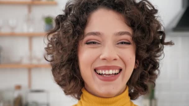 Cerca de la cara sonriendo hispano rizado mujer buscando cámara en casa cocina — Vídeos de Stock