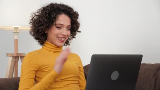 Smiling curly woman student greets talking listens online video call laptop — Stock video