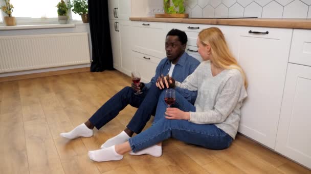 Felice coppia d'amore multietnico parlando con bicchieri di vino rosso seduto sul pavimento — Video Stock