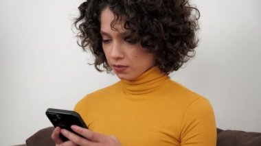 İspanyol kıvırcık kadın öğrenci evde akıllı telefon dinleme ekranı kullanıyor