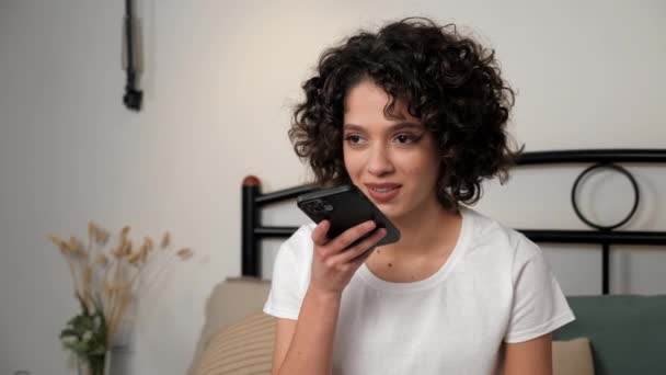 Uśmiechnięta Latynoska kręcona kobieta używa smartfona dyktującego wiadomość audio do przyjaciela — Wideo stockowe