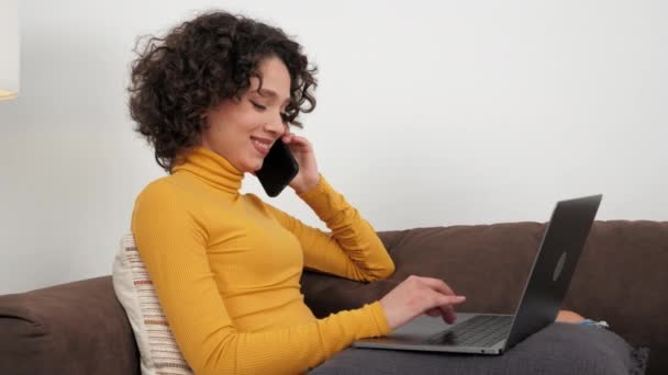 Smiling hispanic businesswoman talking on mobile phone using laptop at home — Stockvideo