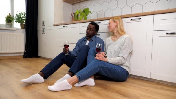 Sorridente famiglia multietnica coppia innamorata parlando bere vino seduto sul pavimento — Video Stock